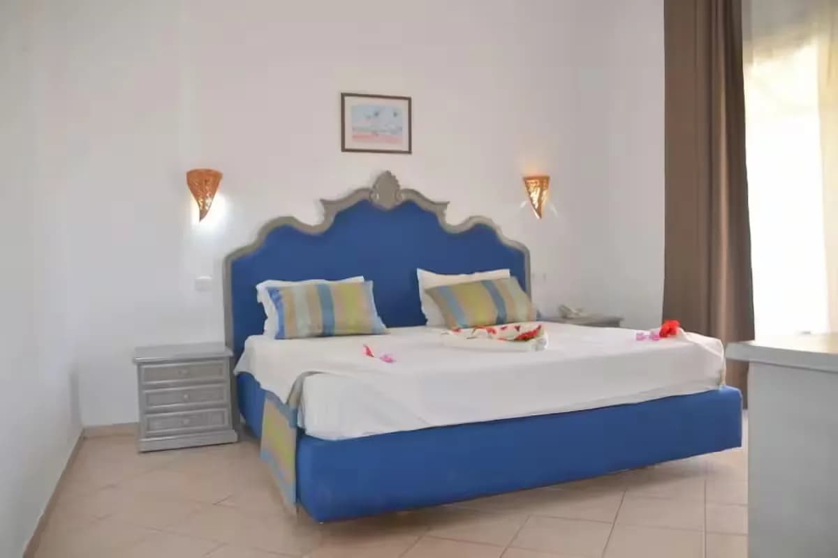 Chambre d’un appartement famille : grand lit, murs blancs, appliques en osier