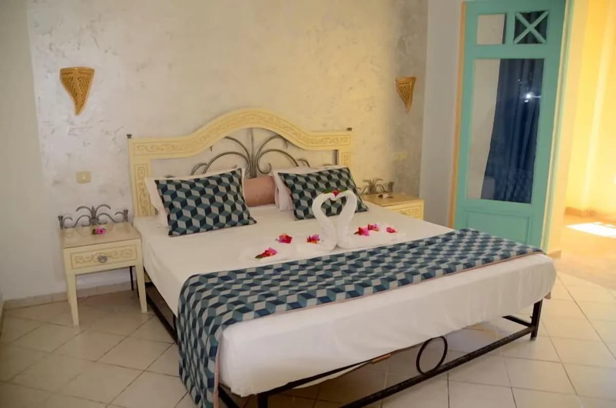Chambre vue jardin : lit double, murs à la chaux, appliques en osier et porte-fenêtre turquoise